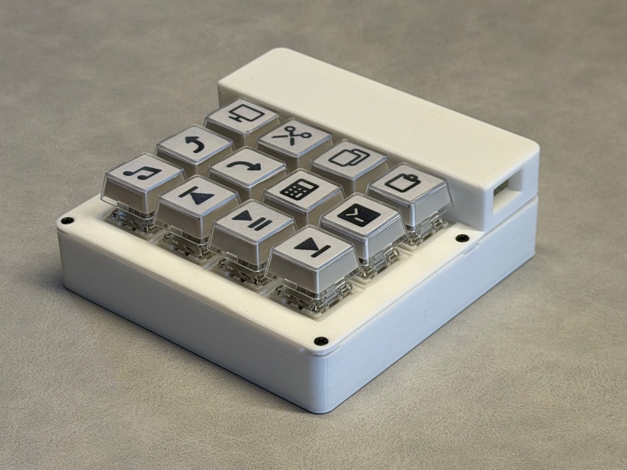 Current STACK prototype with a white enclosure and twelve clear keycaps labelled with shortcuts and media controls.