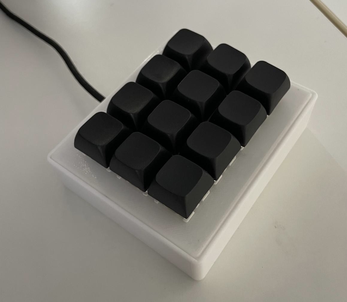 Original STACK V0 prototype with twelve plain black keycaps and a white case.